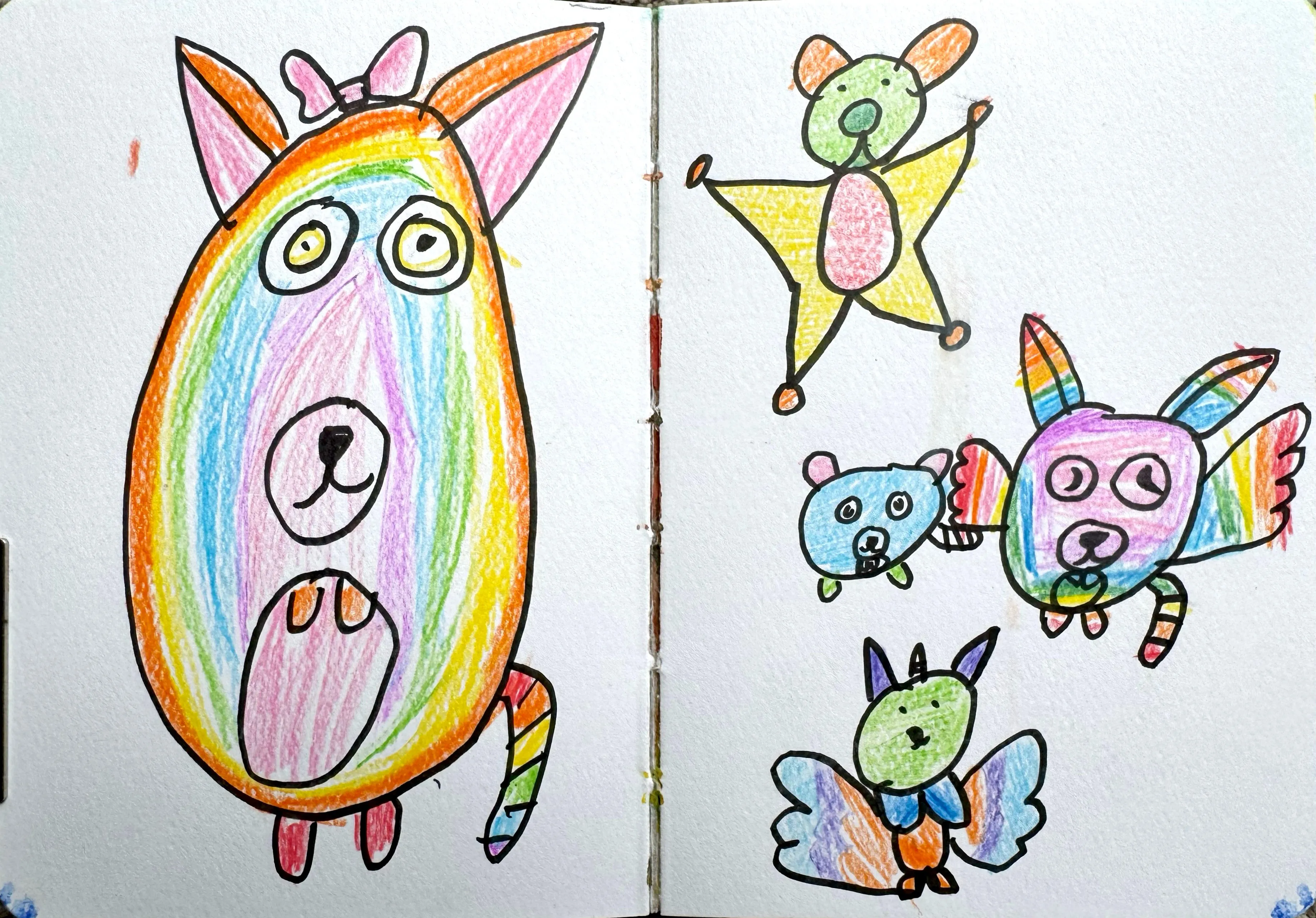 A sketchbook spread filled with whimsical, rainbow-coloured cartoon animal characters drawn in marker and coloured pencil, including a large oval dog, a bear on a star, a blue bear, a purple rabbit with wings, and a green fox-like creature.